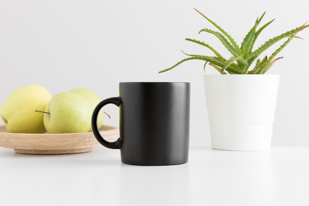 Photo black mug mockup with apples and a aloe vera plant on a white table