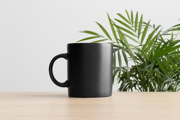 Black mug mockup on the wooden table with a palm plant