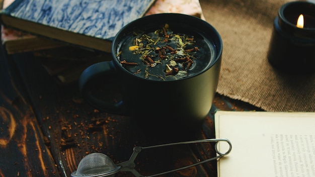 Фото Черная чашка с свежими чайными листьями на воде, написанная на столе с книгами