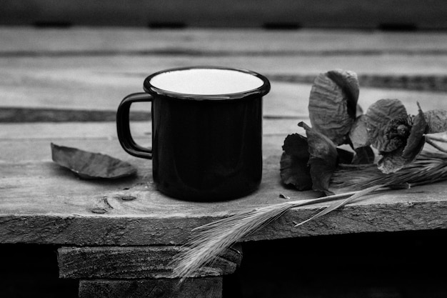 A black mug with a white foam on it sits on a wooden table next to a few leaves.