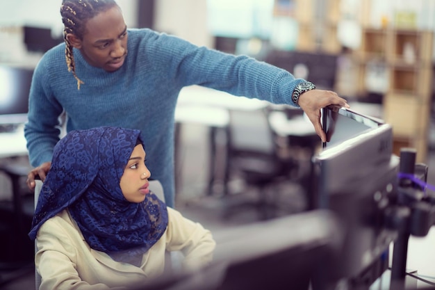 black muslim female software developer working together with her african american male colleague using computer while writing programming code at modern startup office