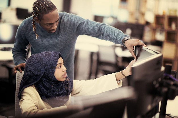 black muslim female software developer working together with her african american male colleague using computer while writing programming code at modern startup office