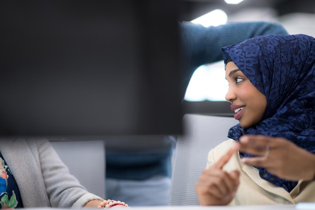 現代のスタートアップオフィスでプログラミングコードを書いている間、コンピューターを使用して彼女の多民族ビジネスチームと一緒に働いている黒人のイスラム教徒の女性ソフトウェア開発者