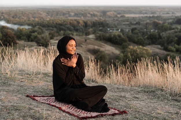 Black muslim woman praying on the carpet. Solat praying on the beautiful hill. Salah traditional pray.