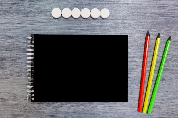 Black notebook with three pencils lie on the table. Notepad with pencils.