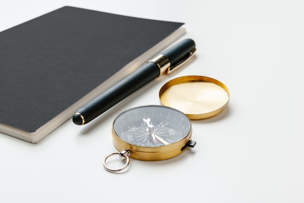 Black notepad for nautical notes and golden compass on a white table