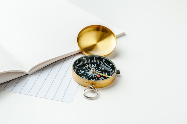 Black notepad  nautical notes and golden compass on a white table