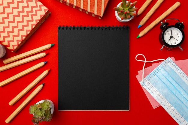 Black notepad page with stationery and medical mask on red background