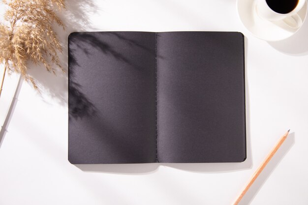 Black notepad with cup of coffee and grass on table