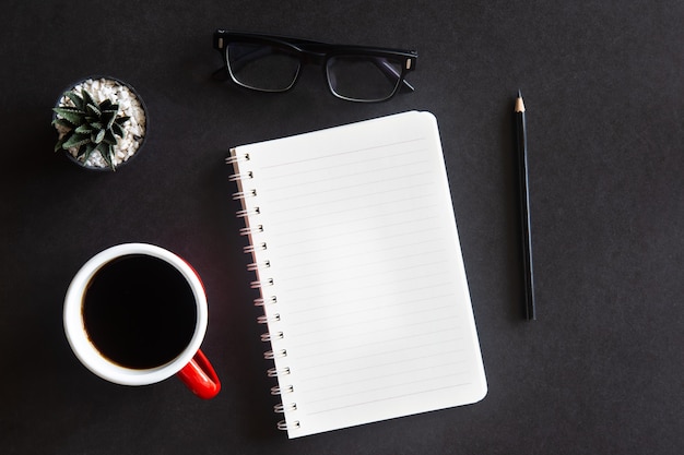 Black office desk with coffee cup, cactus, glasses, pencil and notebook