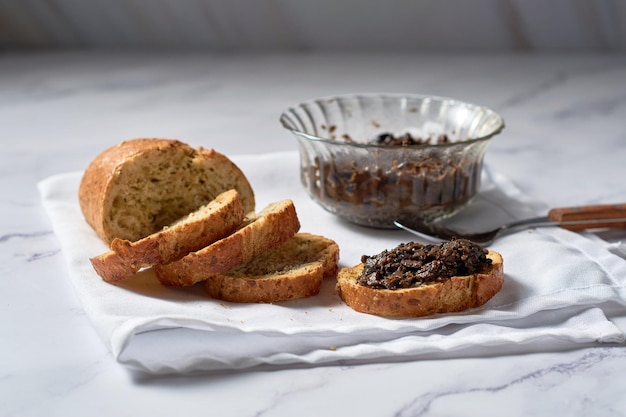 Тапенад из черных оливок в миске с ложкой и хлебом