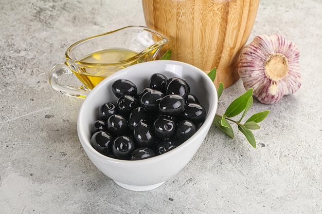 Black olives in the bowl with oil and branch