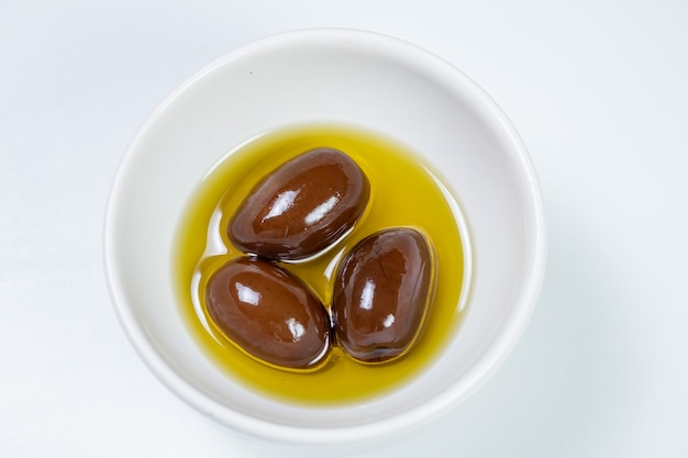 Черные оливки в небольшой запеканке с оливковым маслом на фоне белой поверхности
