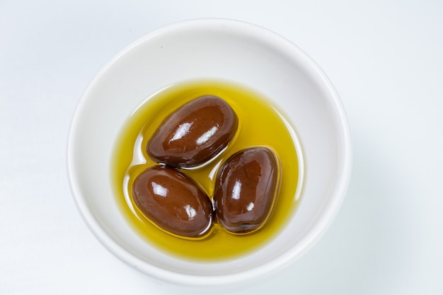 Black olives in a small casserole with olive oil on a white surface background