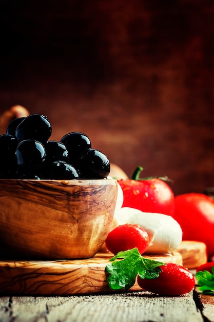 Black olives in a vintage wooden bowl goat cheese tomatoes and wine Still Life with appetizers rustic style selective focus