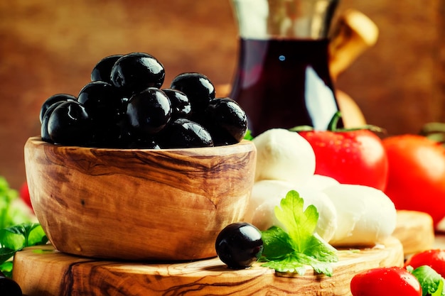 Black olives in a vintage wooden bowl goat cheese tomatoes and wine Still Life with appetizers rustic style selective focus