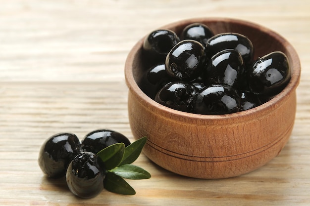 Black olives in a wooden bowl with leaves on a natural wooden table. close-up