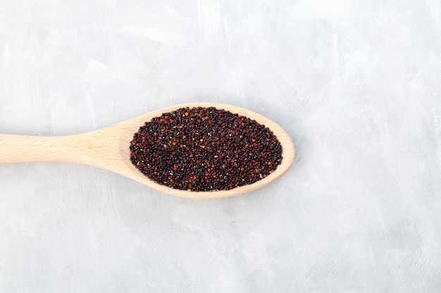 Black organic quinoa or Ragi  millet seeds in wooden spoon top view Grey background copy space