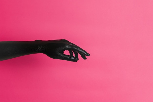 Black painted elegant womans hand on her skin gesticulates on pink background High Fashion art concept