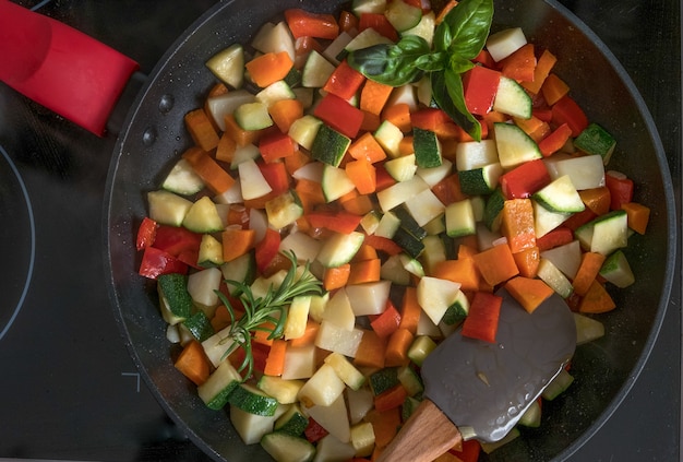 Black pan full of small pieces of potatoes pepper zucchini and carrots to prepare a healthy meal