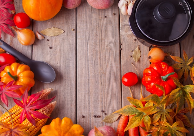 Black pan with autumn leaves and vegetables on the wooden background