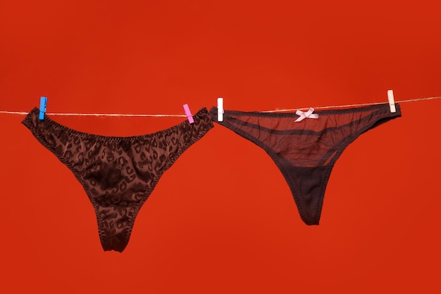 Black panties on rope Sexy lingerie Lace underwear Womans black erotic panties Womens panties hanging isolated on red background