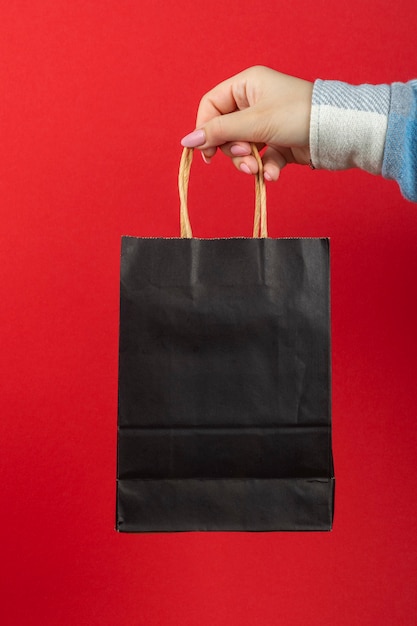 Black paper bag in hand on a red background.