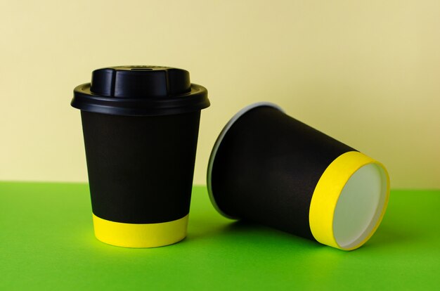 Black paper cup of coffee on green background. 