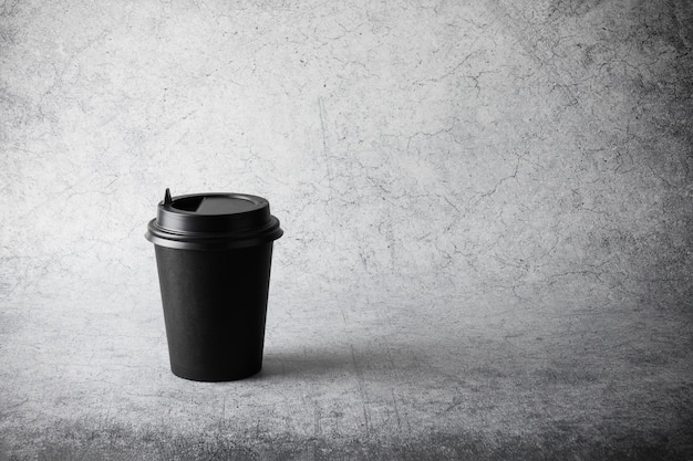 Black paper disposable cup with plastic lid on gray surface