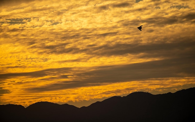 A black paper plane flies over a mountain range.