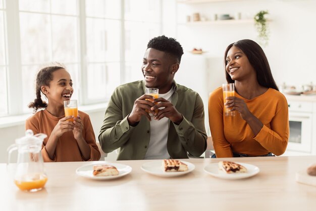 Black parents and daughter having lunch drinking juice at home