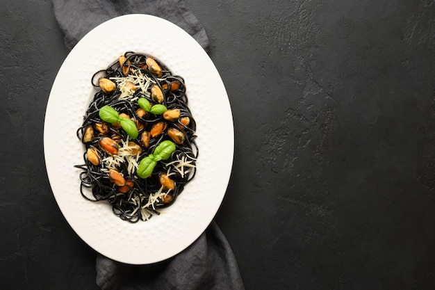 Черные макароны спагетти кальмар Чернила с мидиями в белой тарелке на черном. Вид сверху. Копировать пространство