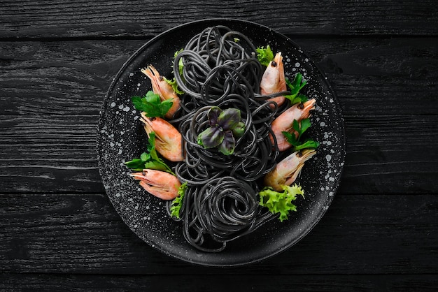 Black pasta with shrimps on a black plate Top view On a black background Free copy space