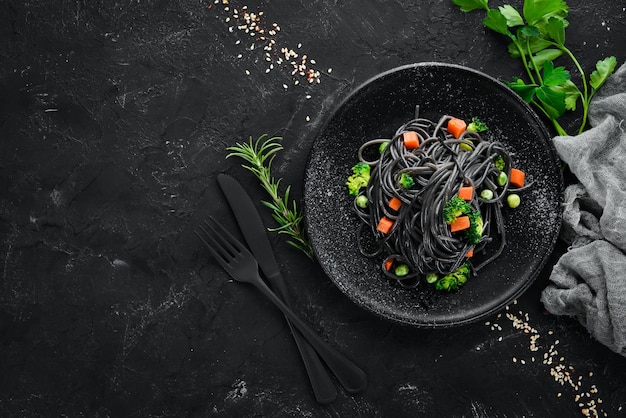 Black pasta with vegetables on a black plate Top view On a black background Free copy space