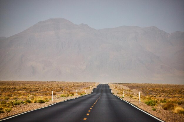 Black paved road leading through sandy desert landscape and mountains