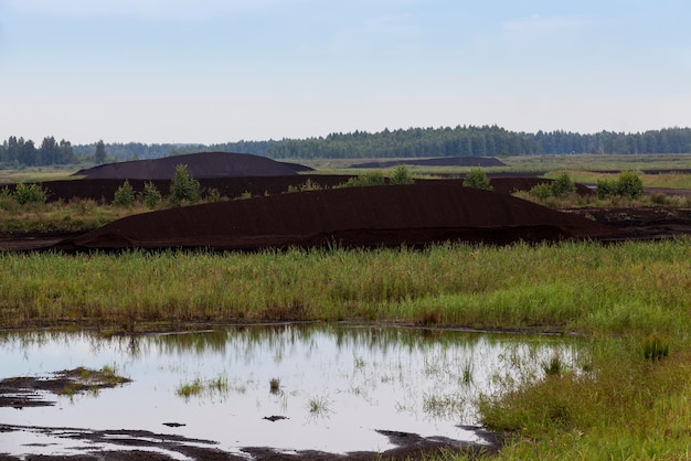 Black peat is stacked in huge piles for loading on transport, the flooded area where peat is extracted