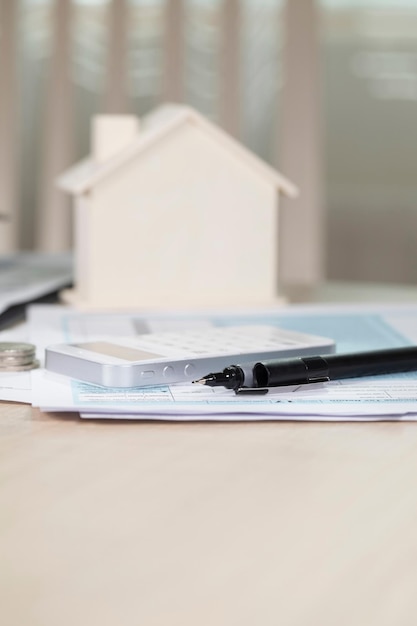 Photo black pen on papers. calculator and small house in the background. closeup