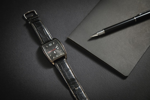 Black pen wristwatch notepad on the black background