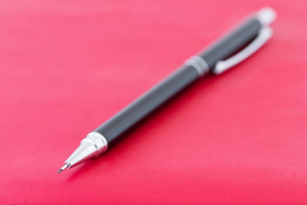 Photo black pencil on the red surface of notebook education concept