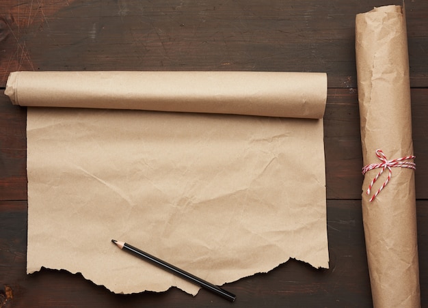 Photo black pencil and roll of untwisted brown paper on a wooden surface from old boards