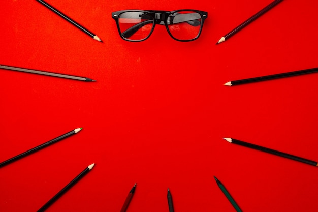 Black pencils and glasses on red background top view, copy space