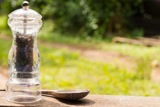 Black pepper bottles and wooden spoon on nature background