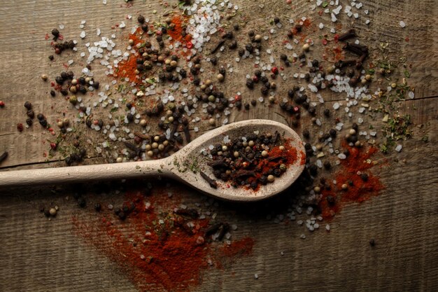 Black pepper peas sea salt red pepper powder spices in a spoon\
on a wooden background