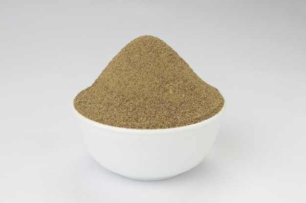 Black pepper powder spices arranged in a white ceramic  bowl with white textured background