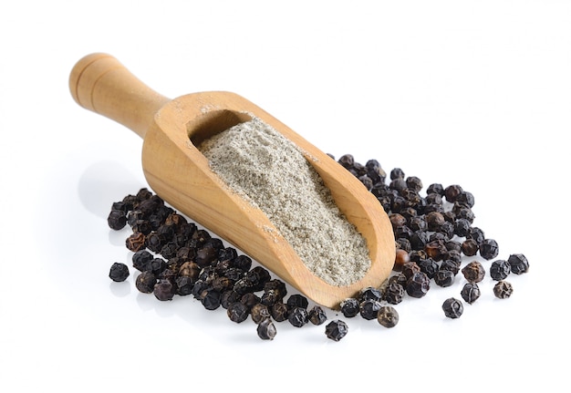 Black pepper powder in wood scoop on white surface