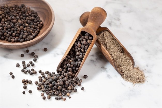 Black pepper seeds and ground peppercorn on marble background. Spices for cooking. Piper nigrum