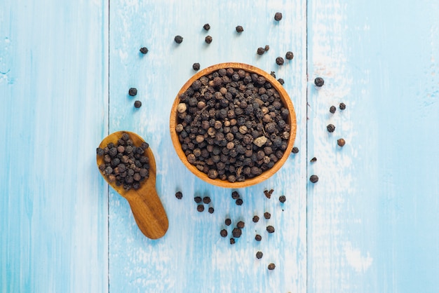 Black pepper in wooden bowl flat lay