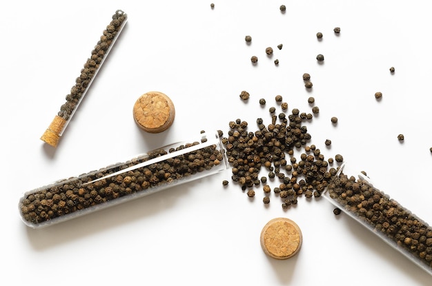 Black peppercorns in glass containers and cork on white background