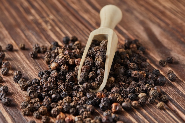 Black peppercorns with wooden spatula are scattered over wooden vintage background.