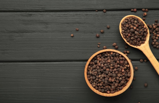 black peppercorns in wooden bowl and spoon on black wooden background space for text